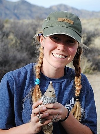 Woman with blonde braids wearing cap and holding a grouse