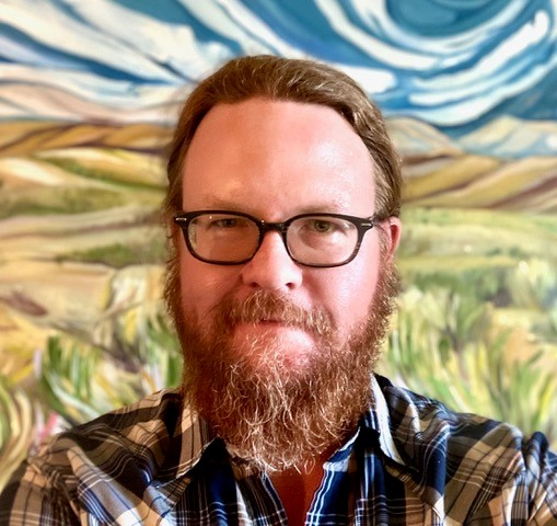 A bearded man with glasses in front of a vivid background image