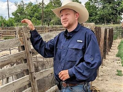 A man in cowboy hat leaning against a rustic wooden fence