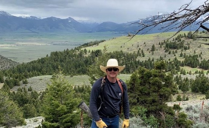 A man is shown holding a hunting rifle in an alpine pasture