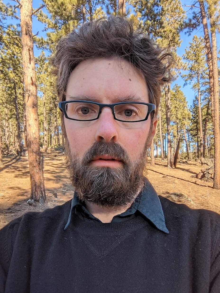 Man with dark hair and beard wearing glasses