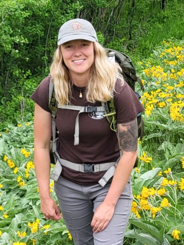 a female graduate student wearing a backpack in an alpine meadow