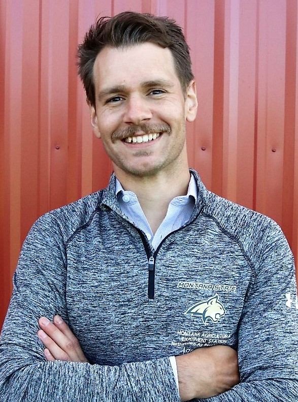 Smiling man with jaunty brown hair standing in front of a barn and wearing an MSU pullover