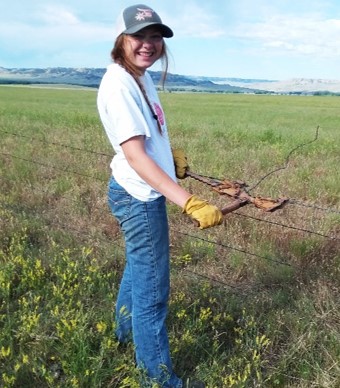 A young woman rancher tying wire in a pasture